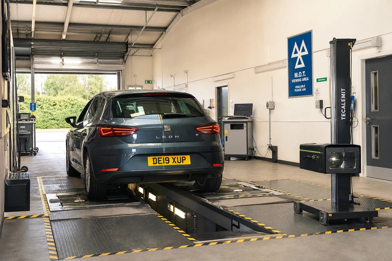 Car positioned over an inspection pit in an MOT testing bay with brake and headlamp testing equipment